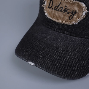 Dettaglio del cappello da baseball in denim invecchiato con ricamo D.daisy e bordi logori