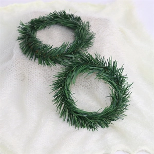 Detail view of two green PVC pine needle mini Christmas wreaths on white plush fabric