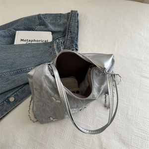 Silver metallic shoulder bag with butterfly charm on a stylish denim layout background
