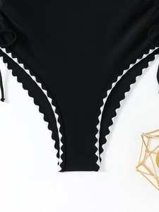 Close-up of black swimwear featuring white scalloped embroidery and side tie details