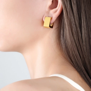 Polished 18K gold geometric square hoop earrings worn by a model in a close-up side view