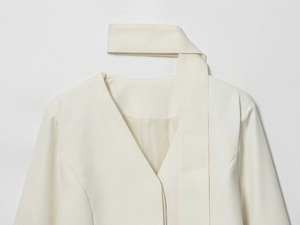 Dettaglio del collo a V e dell'elegante sciarpa su una giacca blazer color panna