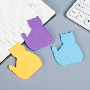 Three cat-shaped sticky notes in purple yellow and blue on an office desk