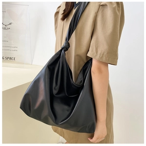 Model wearing a large black minimalist leather tote bag on shoulder in a bright room