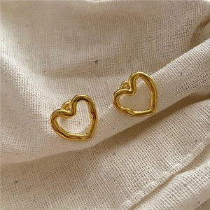 Macro view of gold heart stud earrings featuring irregular textures on linen cloth