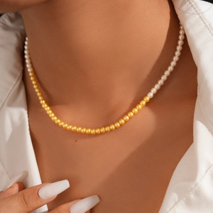 Detail of elegant two-tone pearl necklace showing white and gold beads on a model