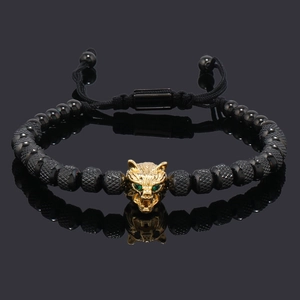 Detail of a golden leopard head charm with green eyes on a black beaded men's bracelet