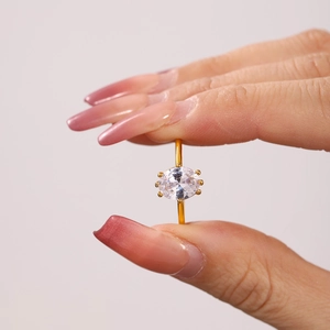 Elegant gold ring with oval zircon center stone held by a hand with manicured nails