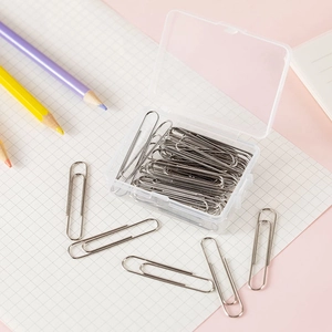 Macro shot of silver metal paper clips in a clear storage box on pink desk surface