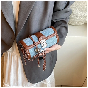 Detail of blue denim cylinder crossbody bag with brown leather trim and metallic sphere charm