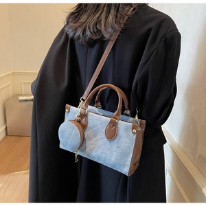 Detail of light blue denim tote bag with leather handles and round coin purse attachment