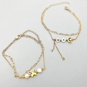 Detail of 18K gold-plated bracelets featuring butterfly, pearl, and evil eye charms