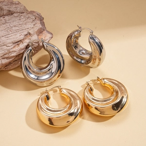 Polished gold and silver chunky hoop earrings with textured finish on beige background