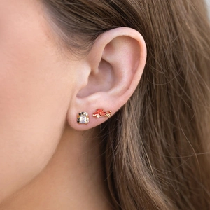 Detailed close-up of zircon earrings and vintage red car studs on model's ear