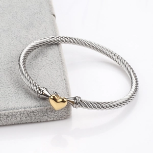 Detail of silver cable bangle with golden heart charm on a gray velvet jewelry display