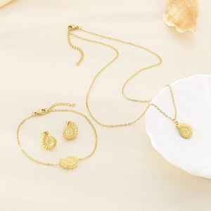 Detailed set of gold conch shell necklace, bracelet and earrings on a neutral fabric background