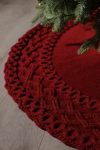 Close-up of red knitted Christmas tree skirt with textured diamond pattern on wood floor