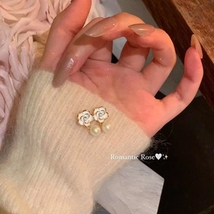 Close-up of elegant camellia earrings with pearls held in hand against floral background