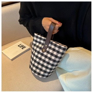 Detail of checkered bucket bag with leather handle held by model against a soft background