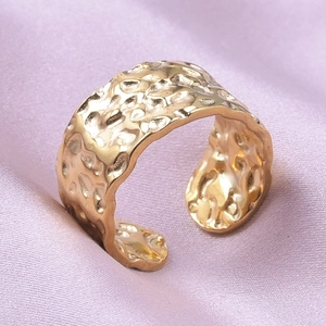 Macro shot of gold-plated wide open ring with irregular hammered texture on purple satin