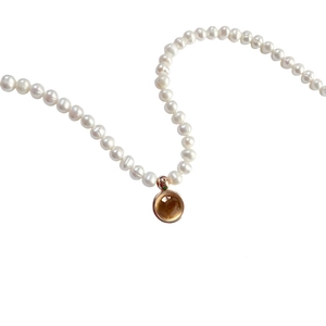 Close-up of elegant white pearl necklace with a vintage golden round birthstone pendant
