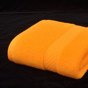 Absorbent thick cotton bath towel in vibrant orange folded on a dark background