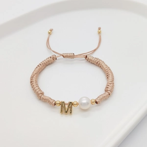 Detail of handmade champagne woven bracelet with letter M gold charm and white pearl