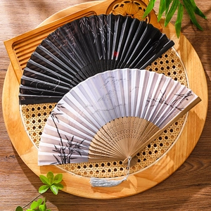 Traditional bamboo folding fans with elegant leaf patterns and classic tassels on a wooden tray