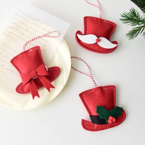 Three red felt Christmas hat ornaments with bow and holly on white background