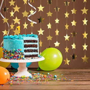 Golden star garland backdrop with a birthday cake and colorful party balloons on a table