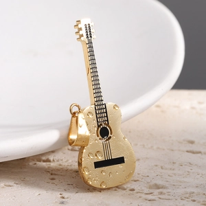 Close-up of golden guitar pendant with water droplets on a white surface