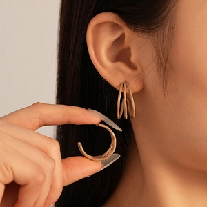 Detailed close-up of multi-layer golden C-shaped geometric hoop earrings on ear
