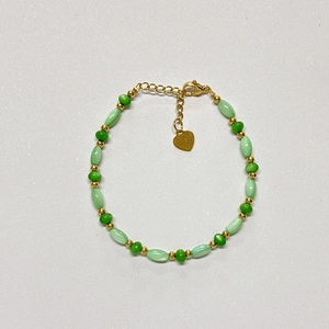 Détail du bracelet avec perles de coquillage vertes et pendentif coeur doré sur la chaîne