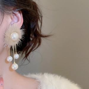 Close-up of pearl earring with beige fur trim and elegant gold chain tassel on model