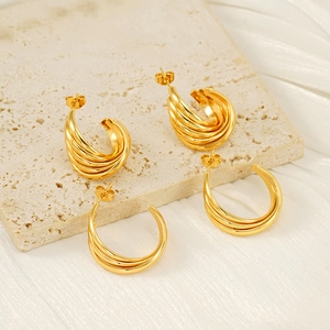 Boucles d'oreilles créoles torsadées plaquées or 18 carats sur un socle en pierre beige