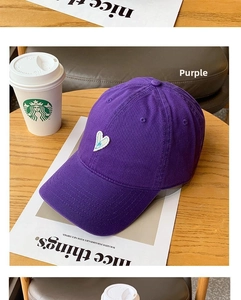 Detail of purple cotton baseball cap featuring a white embroidered heart on a wooden desk