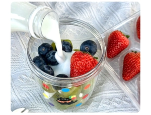Action shot pouring milk into a portable salad cup with strawberries and blueberries