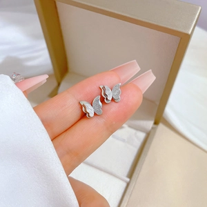 Macro detail of double-layered butterfly stud earrings with matte and polished finish