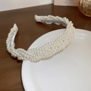 Detail of cream white faux pearl braided headband resting on a ceramic plate