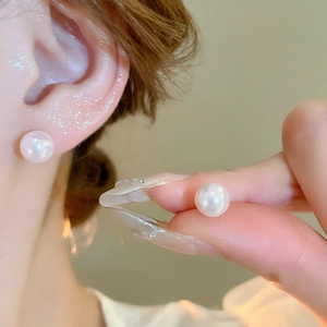 Close-up of minimalist white pearl stud earrings with elegant luster on female model