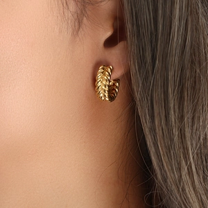 Detail of gold wheat grain pattern C-shaped earrings worn by a model for size visual