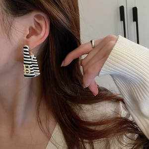 Close-up of black and white striped C-shaped earrings with gold letter B on a model
