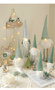Close-up of glowing LED Christmas gnomes in sage green and silver on a soft knit blanket