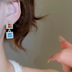 Gros plan de boucles d'oreilles carrées avec pierres ambre et cyan dans un serti halo