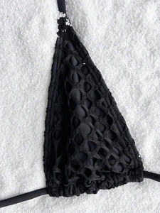 Detail of black bikini top with textured mesh fabric over solid lining on white sand