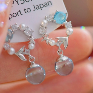 Macro view of ocean-themed mermaid tail earrings with blue zircons and hanging spheres