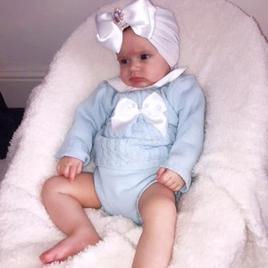 Detail of baby knit outfit in sky blue featuring a large white satin bow and gemstone hat