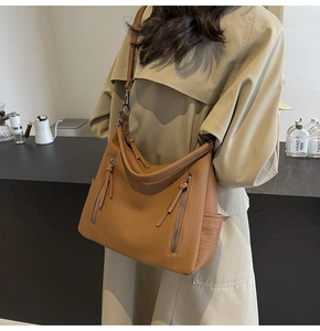 Brown soft leather hobo bag with side zippers shown on a model in a trench coat