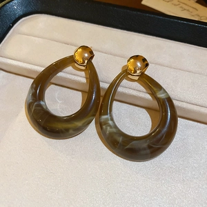 Macro view of brown resin hollow teardrop earrings on a beige velvet jewelry box