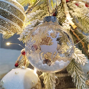 Transparent 8cm Christmas ball with white deer and snowflakes hanging on a festive tree